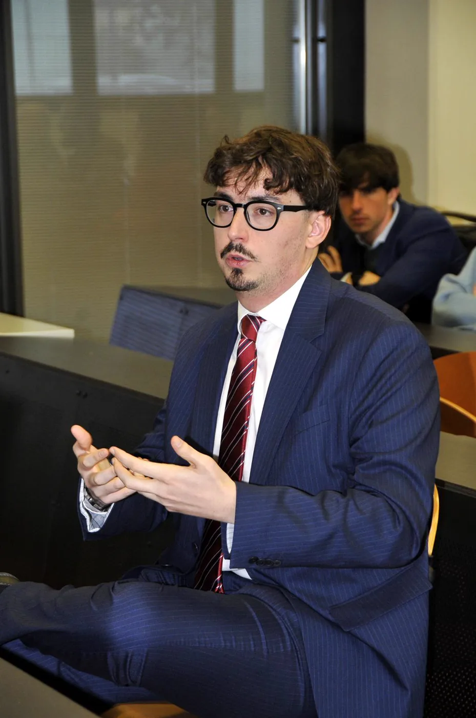 Alessandro Soldà, in giacca e cravatta, spiega qualcosa con le mani durante un incontro in aula